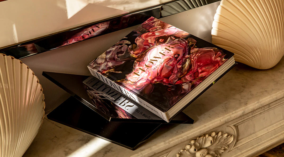 Libro Assouline Flowers en una mesa elegante, reflejado en espejo, añadiendo lujo y arte a la decoración.