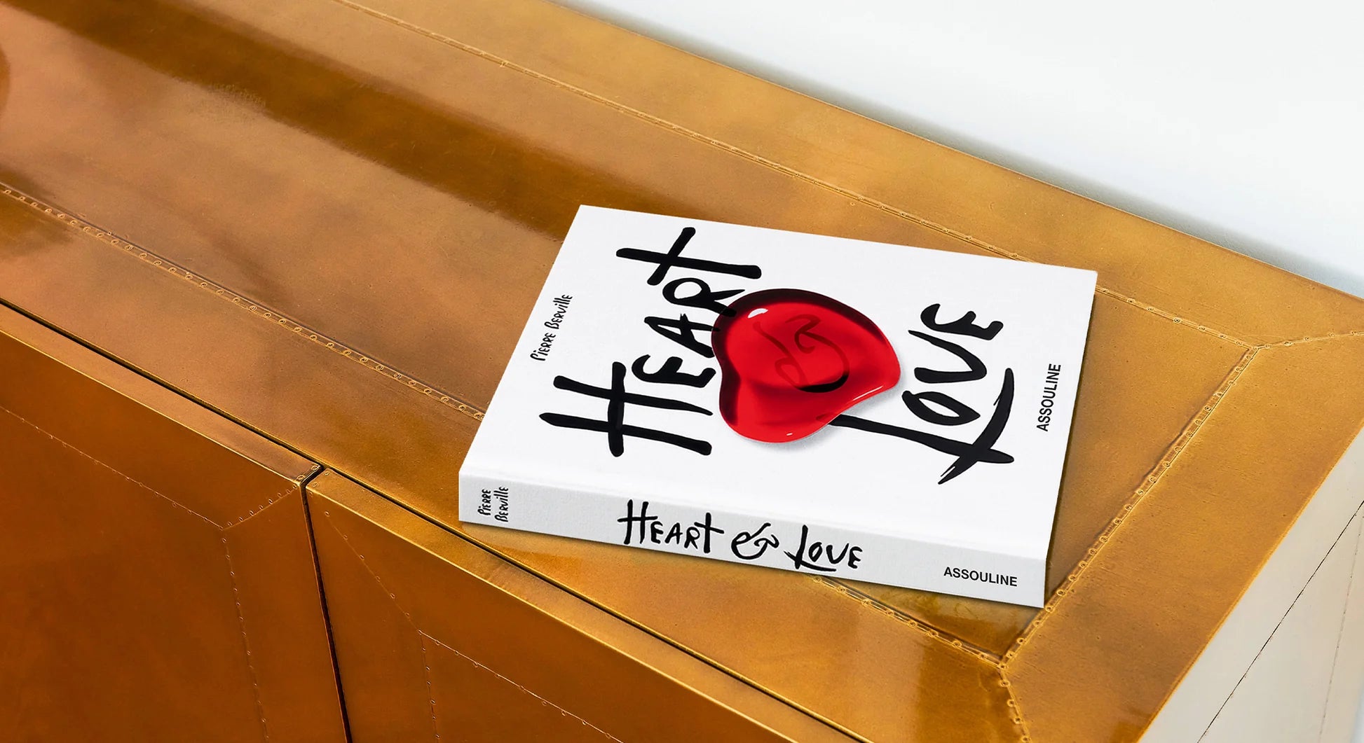 Libro de mesa Assouline Heart & Love posado elegantemente sobre un mueble de madera lacada en bronce.