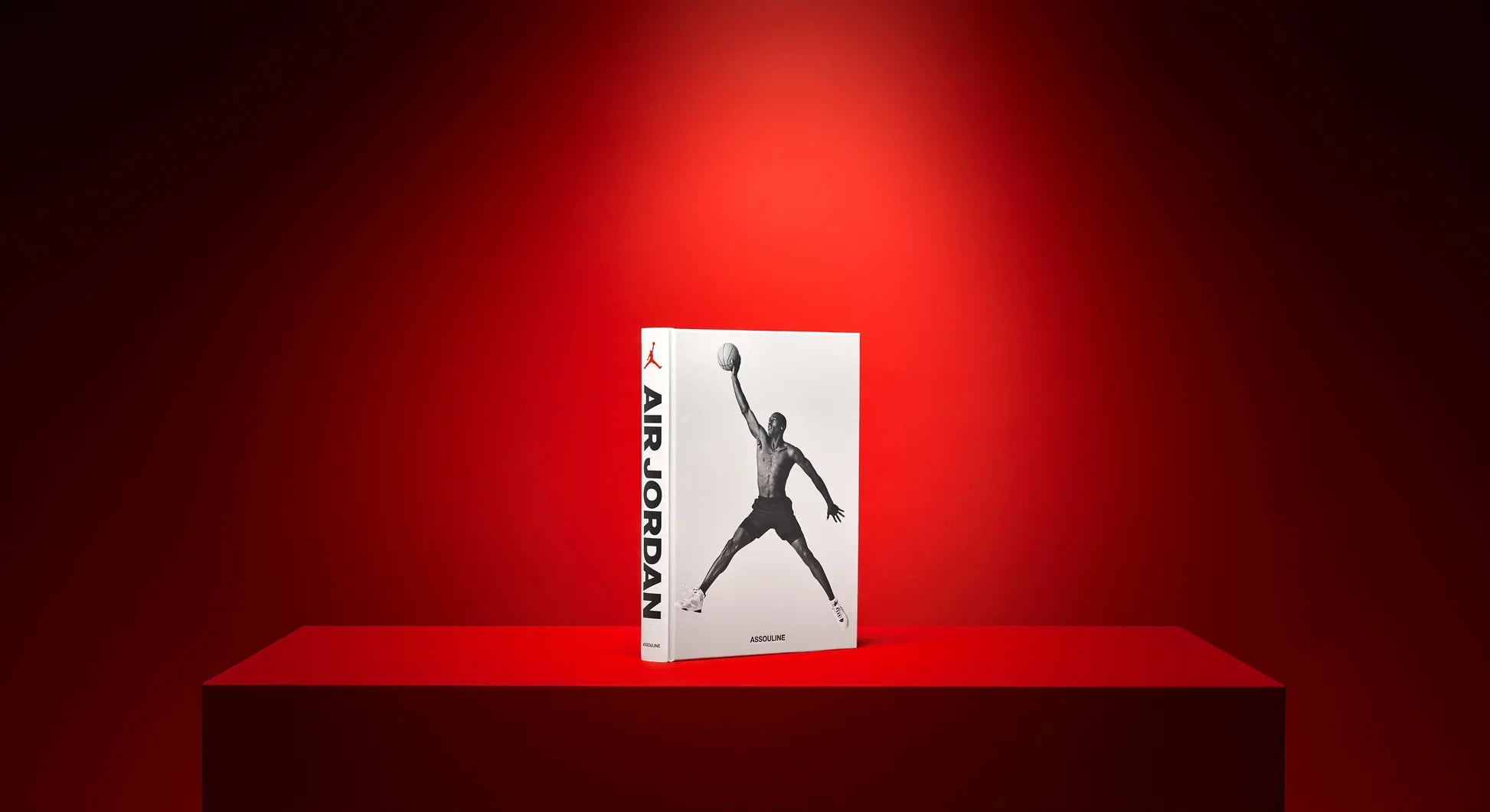 Libro Assouline Air Jordan Classic exhibido elegantemente en un pedestal rojo con iluminación destacada.