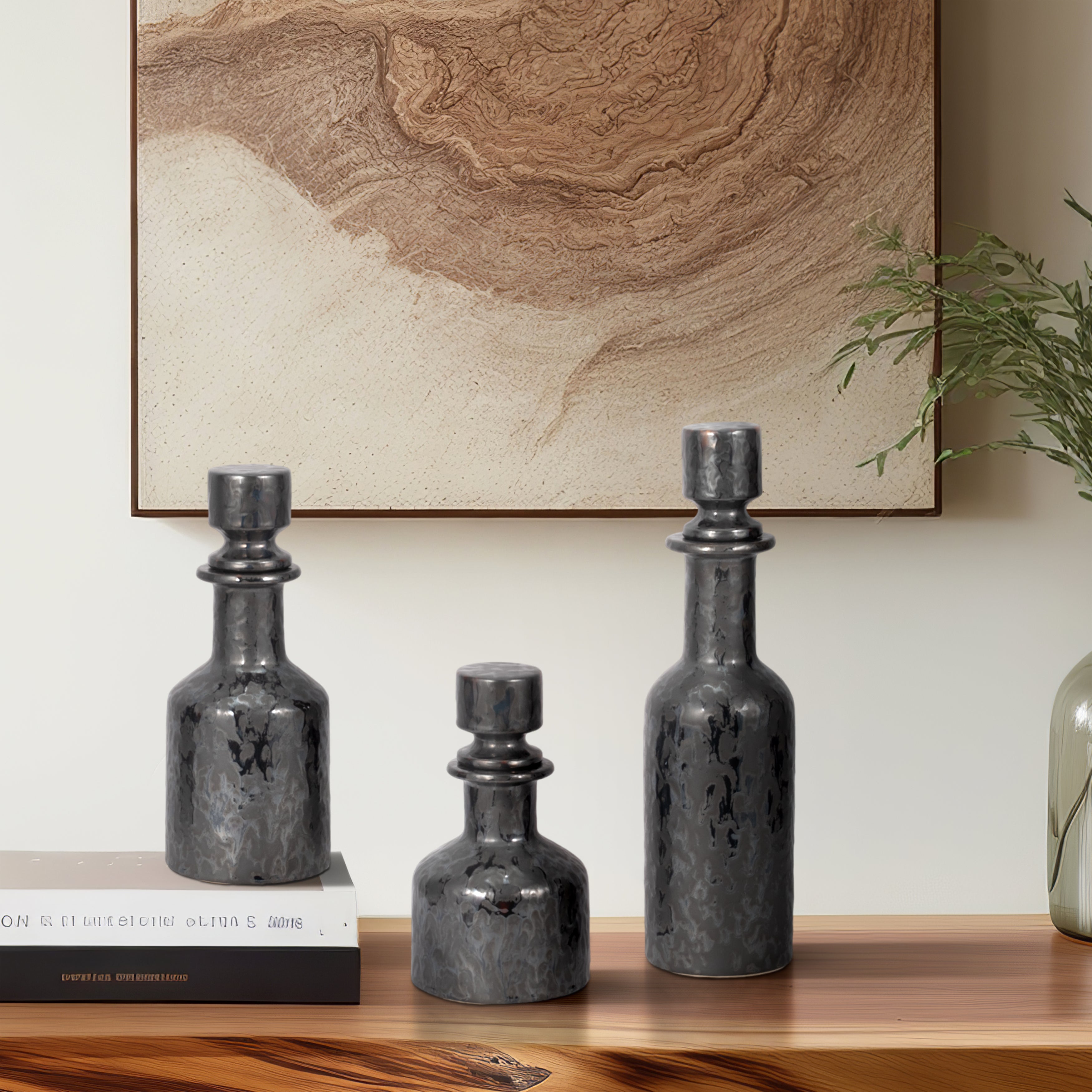Conjunto de tres botellas decorativas martilladas oscuras de distintos tamaños sobre una mesa de madera.