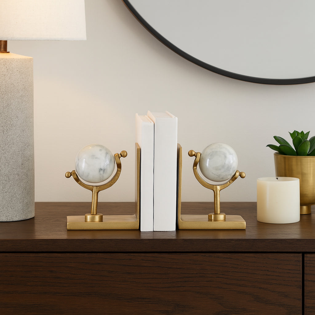 Sujetalibros de mármol y acabado dorado en un ambiente decorado, junto a libros, lámpara y vela.