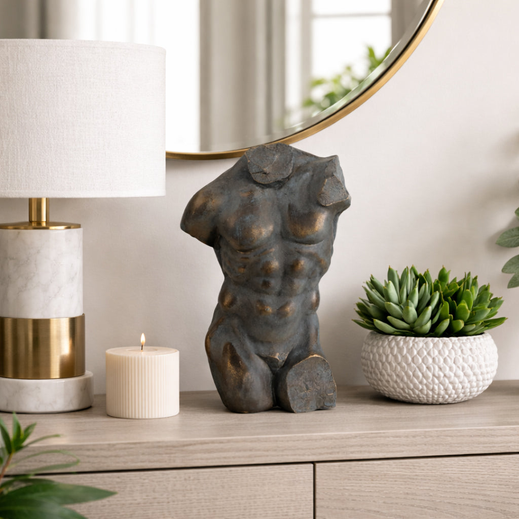 Escultura de torso masculino decorando una cómoda moderna, junto a lámpara y planta, ambiente elegante.