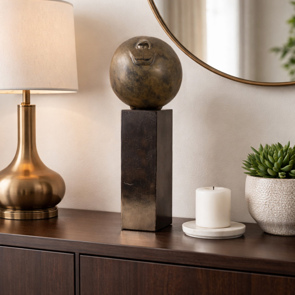 Escultura esférica de bronce en ambiente lujoso, mesa de centro con lámpara y espejo dorado. Decoración sofisticada.