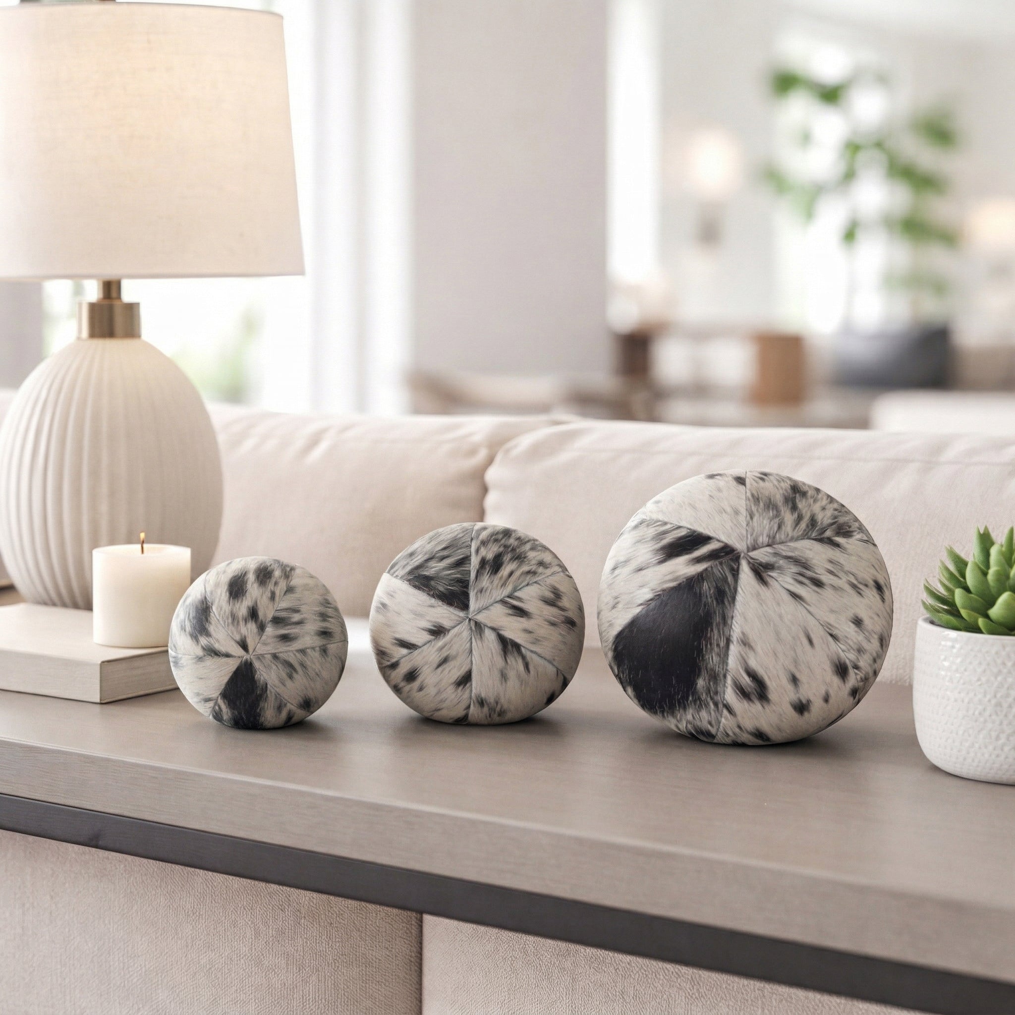 Esferas decorativas cowhide en sala moderna, adornando una consola junto a lámpara y planta.
