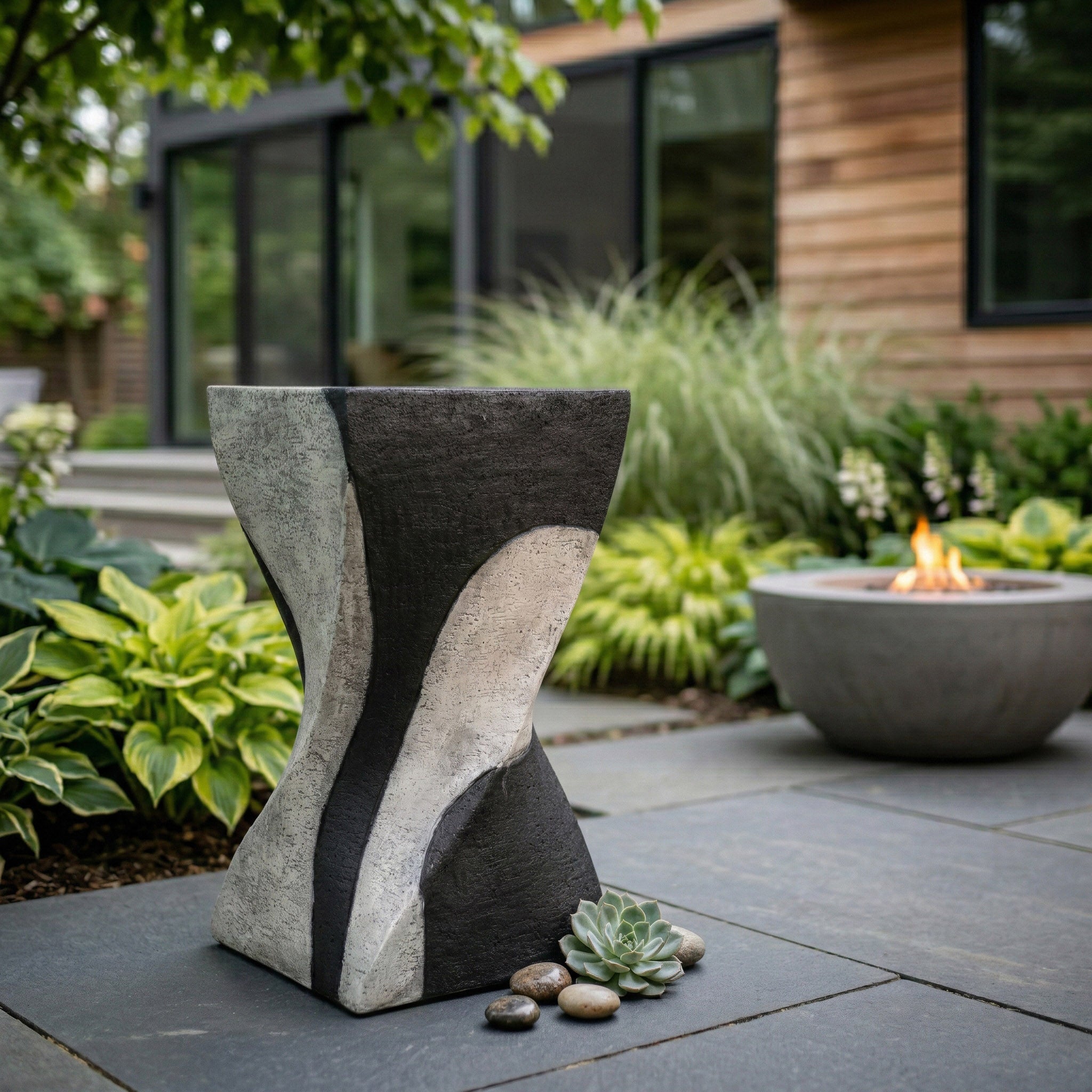 Mesa auxiliar escultural bicolor de concreto en patio moderno con fogata y vegetación.