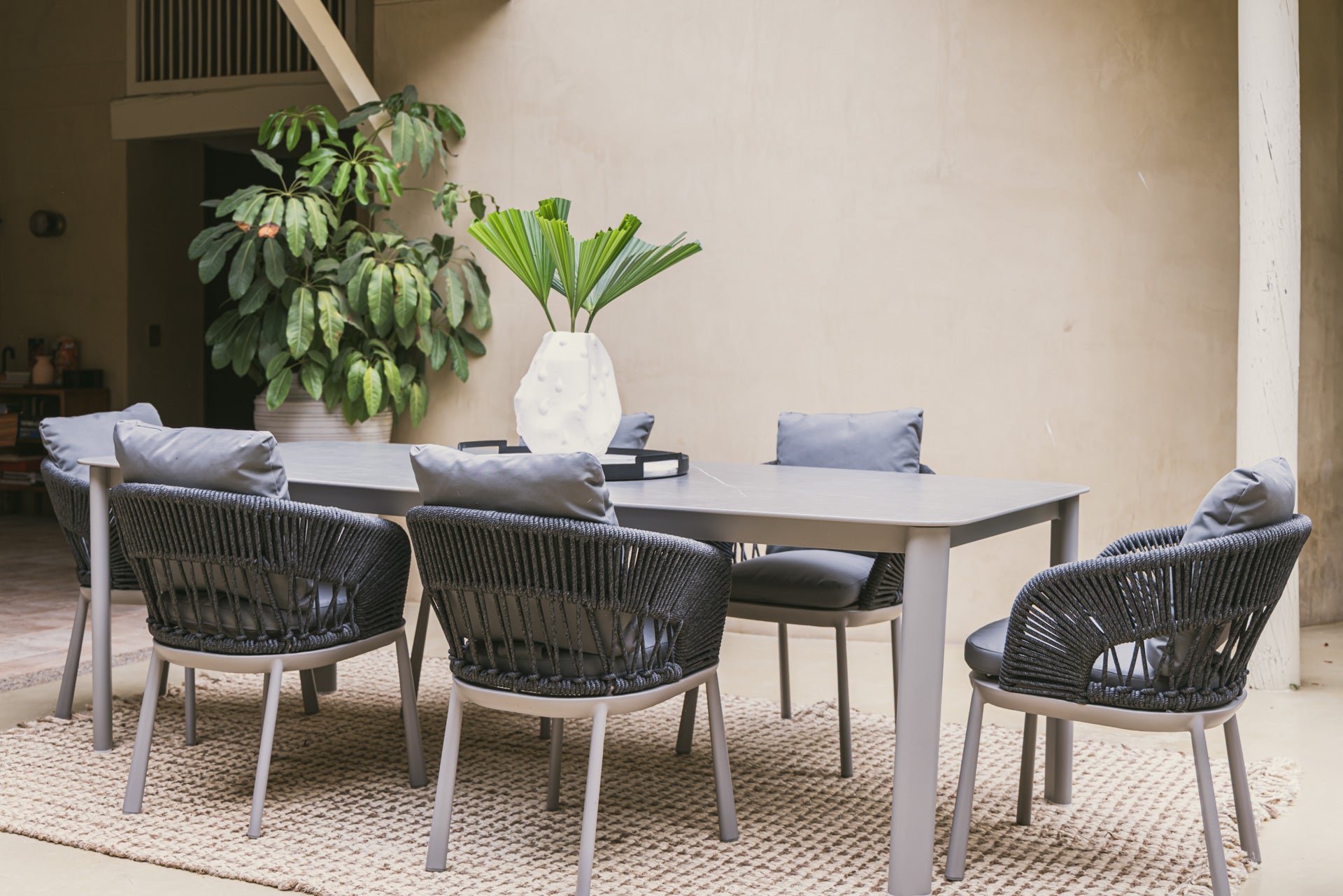Conjunto de mesa comedor exterior moderna y sillas en patio rodeado de vegetación.