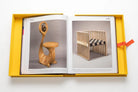 Páginas abiertas del libro Assouline, mostrando dos sillas icónicas de diseño en estuche amarillo.