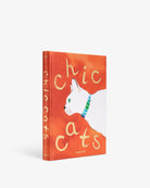 Libro decorativo Assouline Chic Cats de pie, mostrando lomo y portada con gato blanco y collar vibrante.