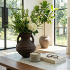 Jarrón decorativo con arreglos florales en una sala de lujo con ventanales grandes y mesa de mármol.