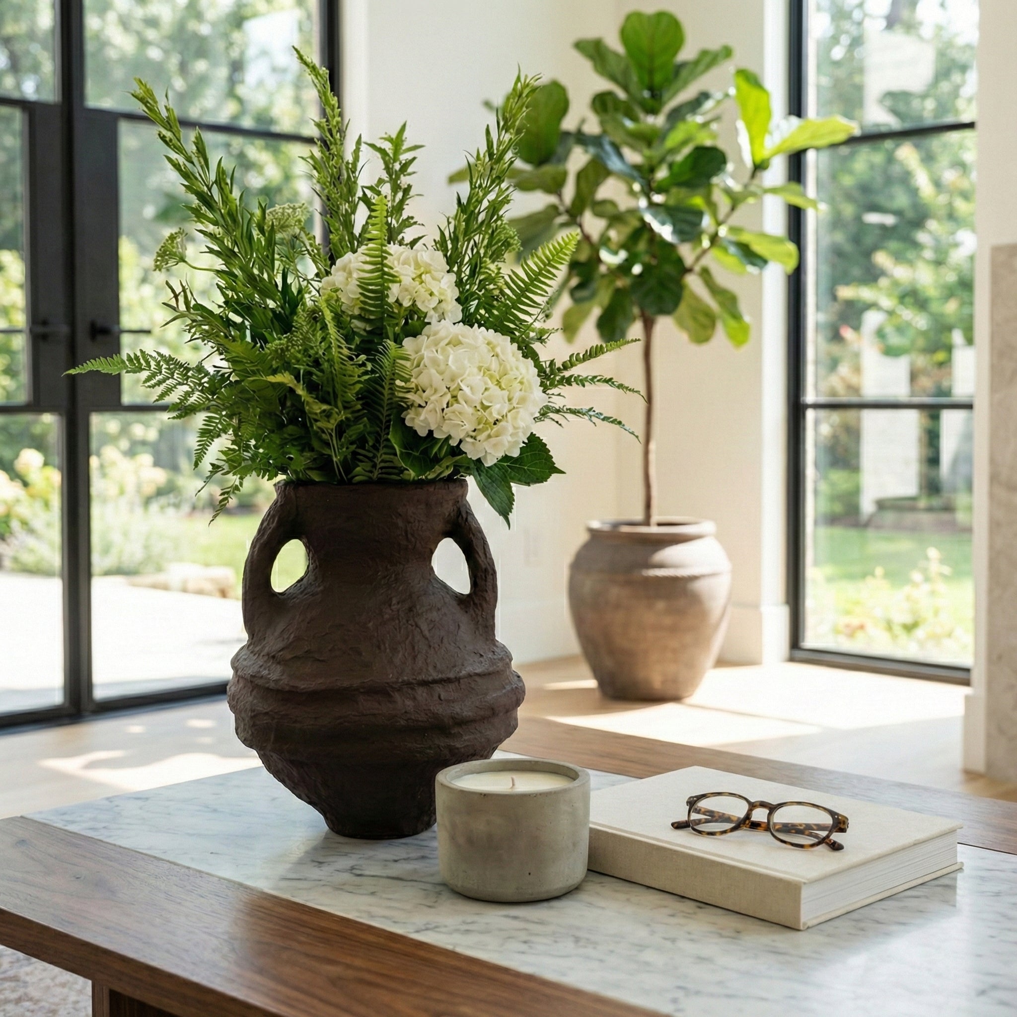 Jarrón decorativo con arreglos florales en una sala de lujo con ventanales grandes y mesa de mármol.
