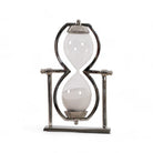 Reloj de arena decorativo de lujo en metal cromado y arena blanca, sobre fondo blanco.