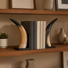 Sujetalibros de cuerno natural adornando una estantería de madera con libros y objetos decorativos.