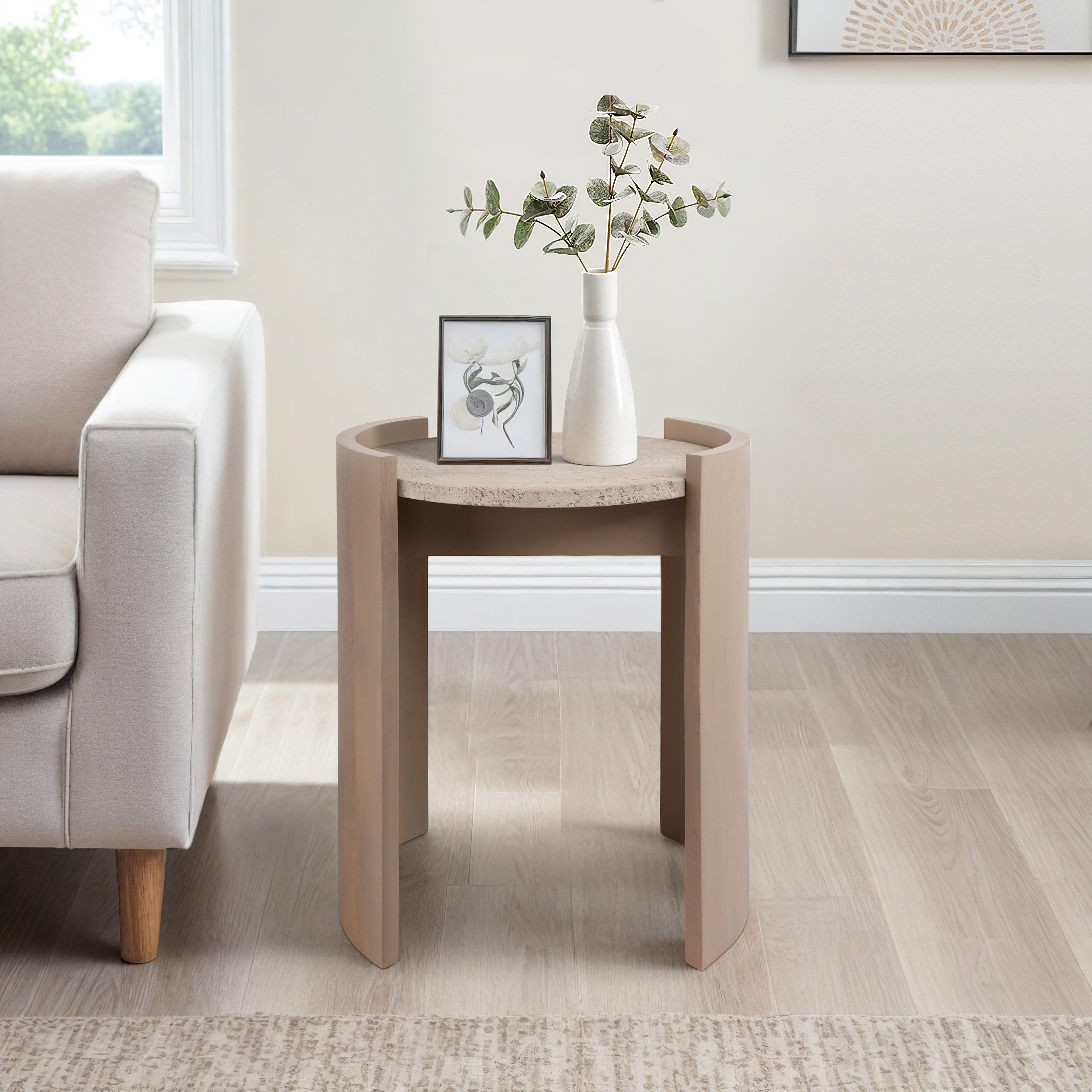 Mesa auxiliar moderna en madera y piedra junto a un sofá beige, decorada con un marco y un jarrón en una sala elegante.