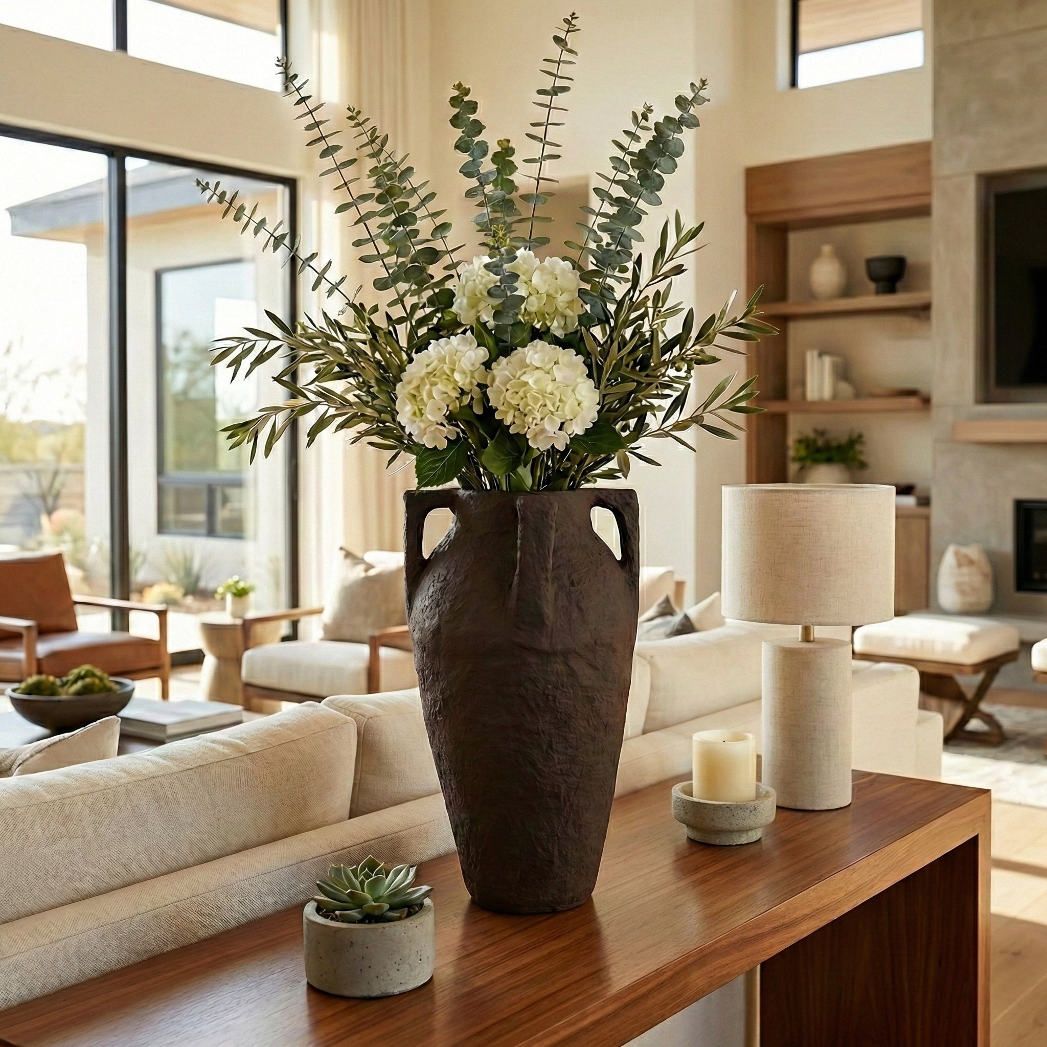 Jarrón marrón grande en sala de estar moderna con sofás blancos, flores blancas y eucalipto.
