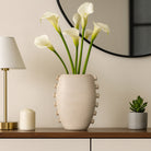 Jarrón cerámico beige en un ambiente de sala elegante con calas blancas y detalles de lujo.