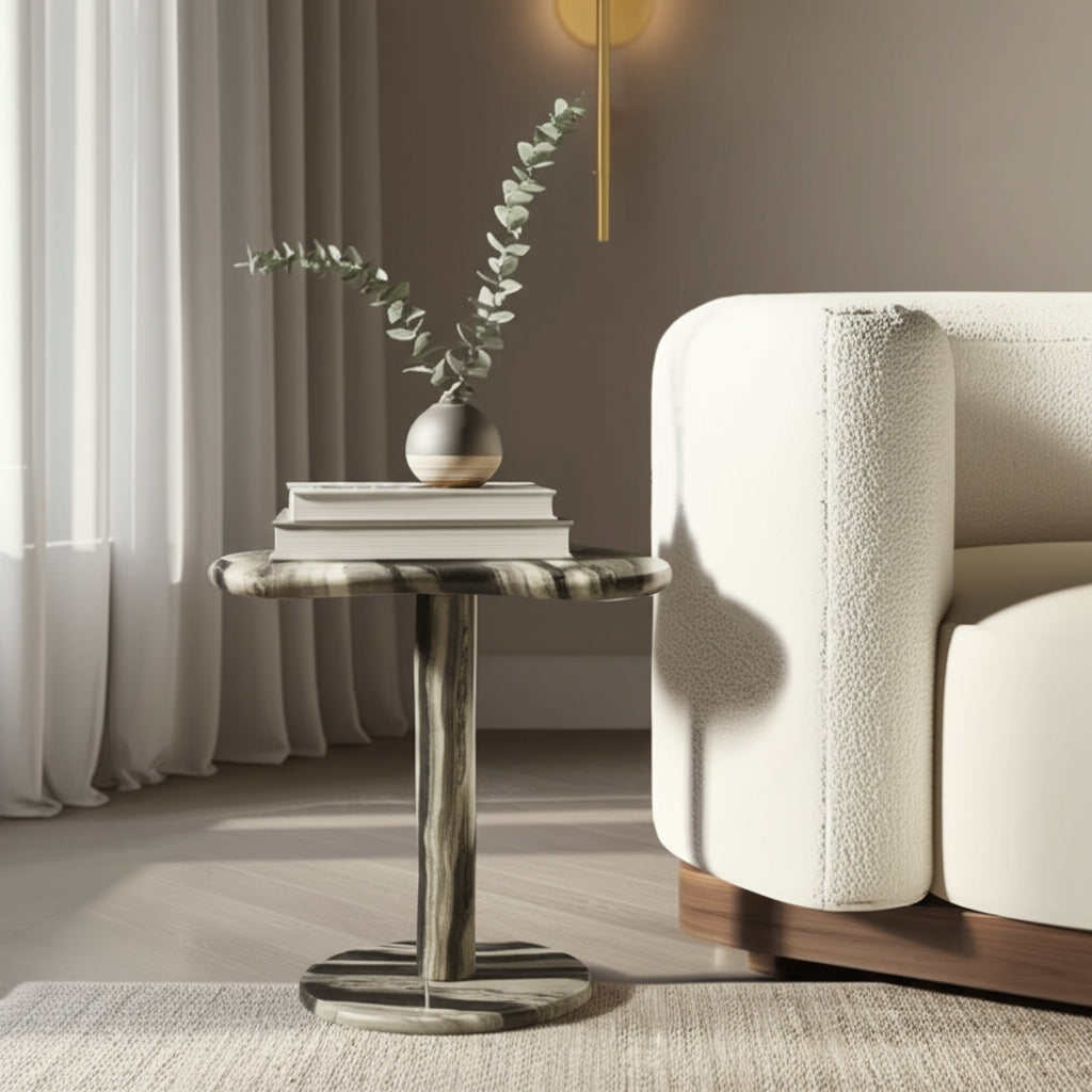Mesa auxiliar de piedra blanco y negro junto a sofá blanco, decorada con libros y jarrón minimalista.