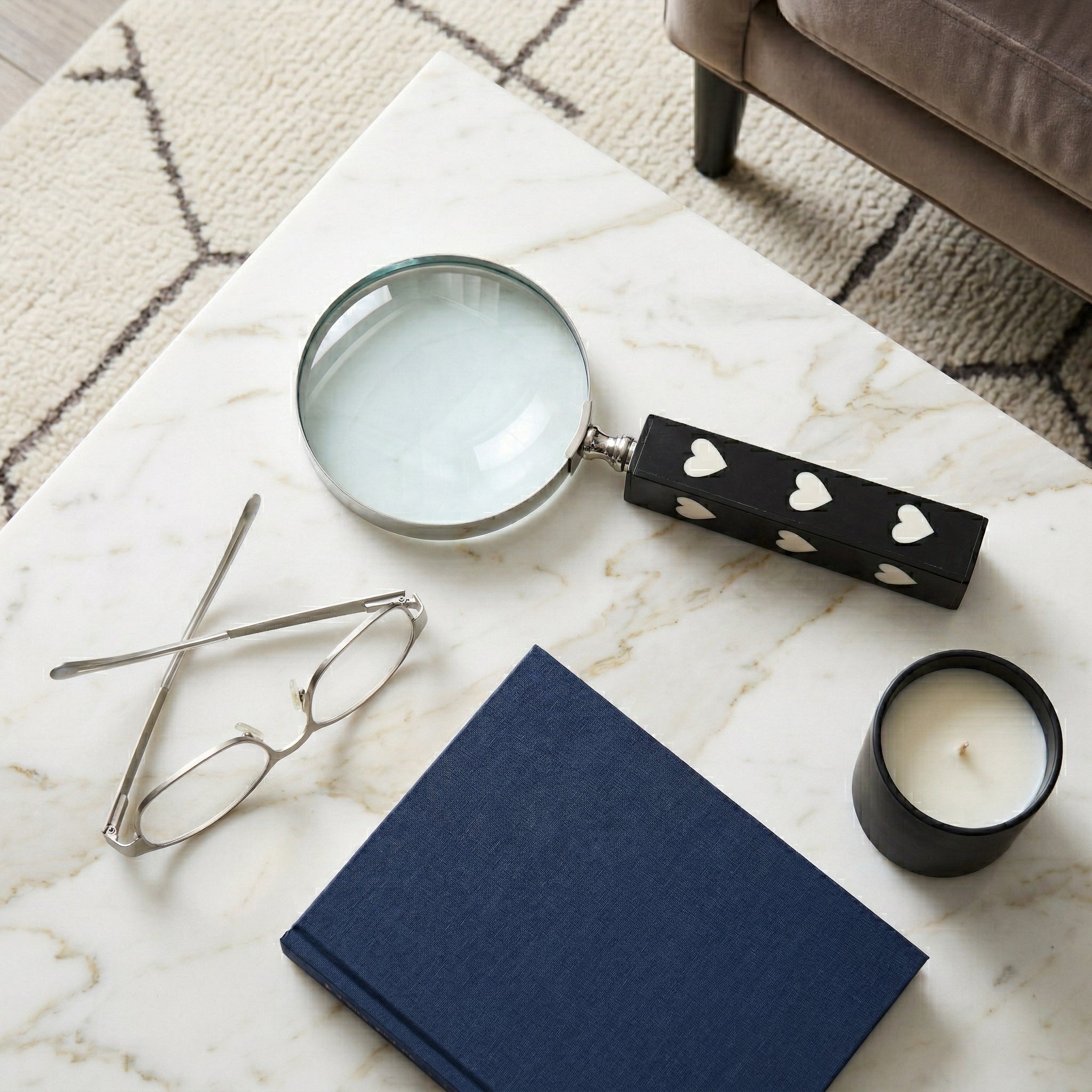 Lupa decorativa con corazones sobre mesa de mármol, junto a libro y gafas, realzando el estudio con estilo.