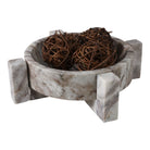 Bowl de mármol con base elevada y esferas decorativas de ramas secas en su interior, sobre fondo blanco.