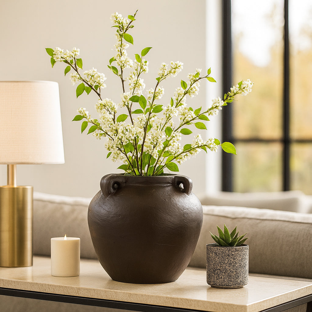 Jarrón marrón oscuro con flores blancas en una mesa de sala moderna.
