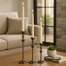 Juego de tres candelabros metálicos con velas encendidas decorando una mesa de sala de estar.