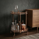 Elegante carro bar con bebidas, decantadores y copas en sala de estar moderna, tono bronce.