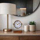 Reloj de mesa decorativo en un ambiente moderno con lámpara, espejo y planta, realzando la elegancia del hogar.
