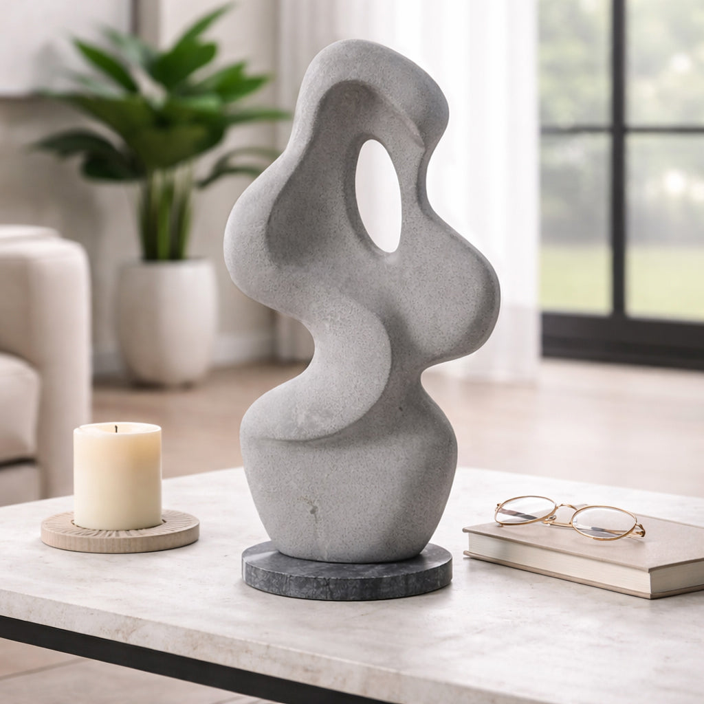 Escultura decorativa abstracta gris en una mesa de centro de sala moderna, con vela y libro, ambiente de lujo.