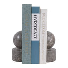 Par de sujetalibros de mármol gris con libros de diseño organizando una estantería moderna.