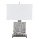 Lámpara de mesa moderna con base cilíndrica y pantalla textil clara, iluminando un espacio con luz cálida