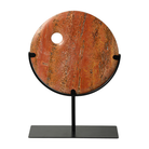 Escultura circular de mármol rojo veteado con orificio, exhibida en base de metal negro, estilo