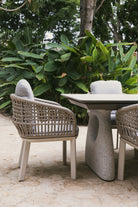 Sillón de terraza en cuerda acrílica y aluminio junto a mesa moderna en jardín tropical.