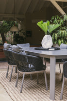 Detalle de mesa comedor exterior de piedra sinterizada en patio con sillas de cuerda y decoración.