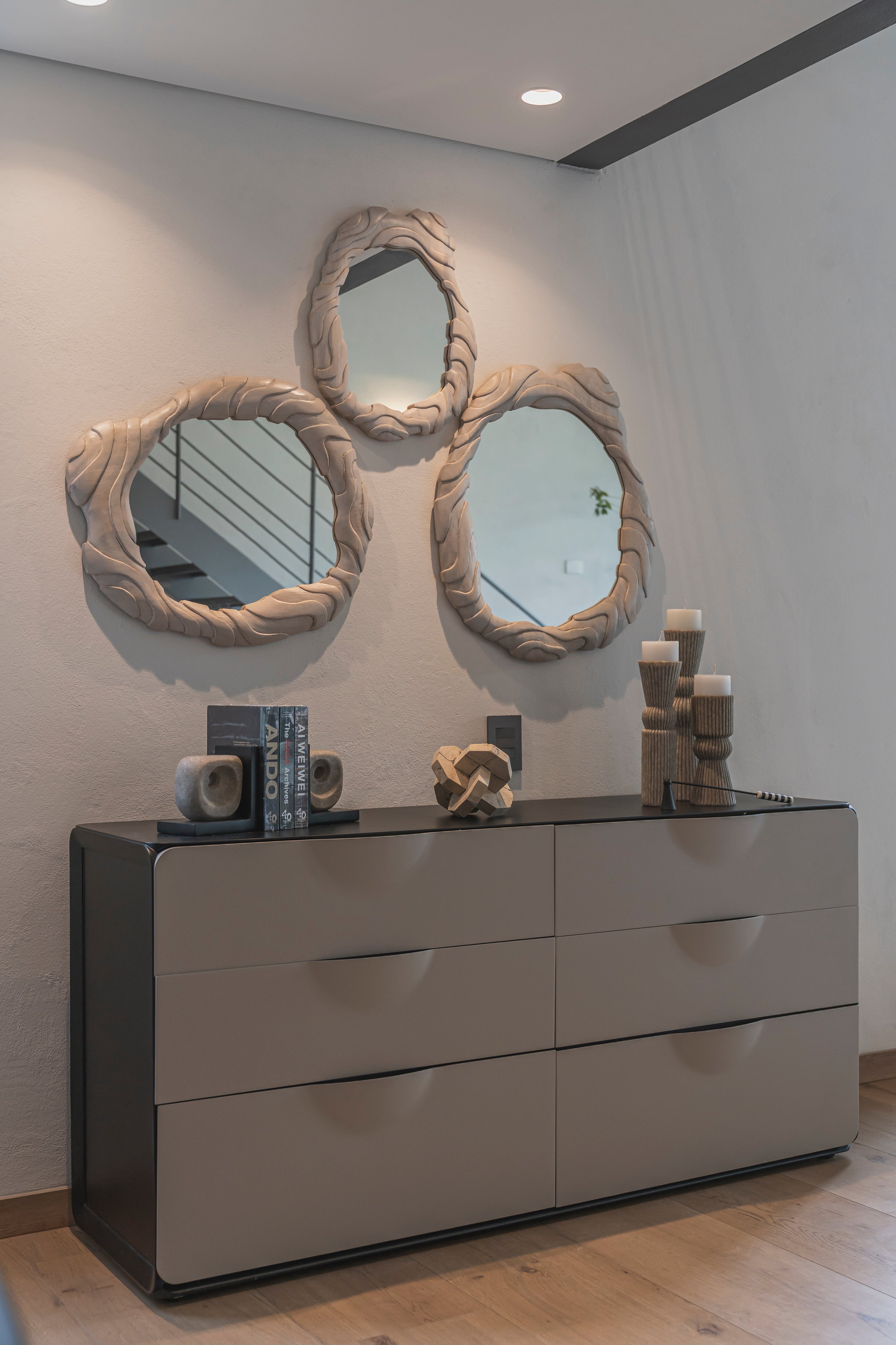 Sujetalibros de piedra y base negra decorando una cómoda con espejos orgánicos y velas en un interior moderno.